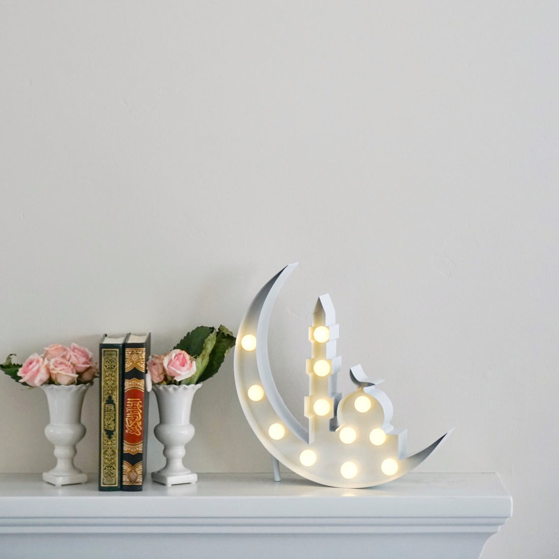Crescent marquee next to qurans and flowers on a shelf